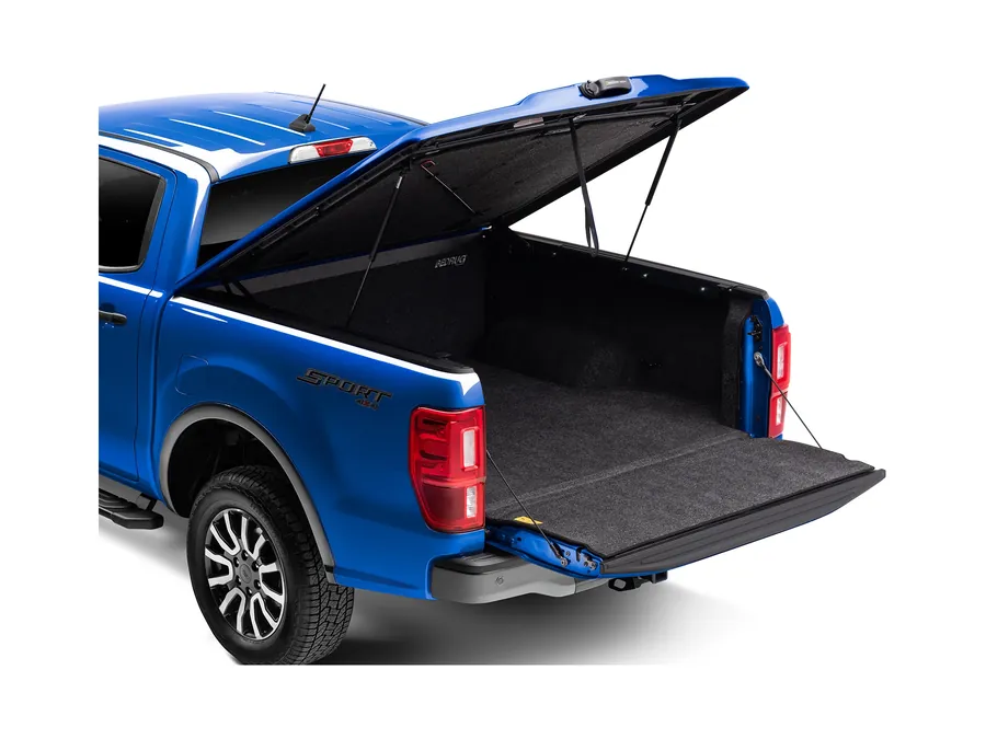Hard one-piece bed cover raised on gas struts over the bed of a blue pickup, rear three-quarter view with the tailgate down